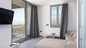A modern bedroom with a large sliding glass door leading to a balcony, a flat-screen TV mounted on the wall, a beige sofa, and a small table with two bowls. - Kōa Villa I, idyll Seaview Near Beach by etouri (Heraklion)