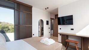 A modern hotel room with a large bed, a desk, a TV, and a balcony with a view of the hills. - Kōa Villa II, Stylish villa Near Beach by etouri (Heraklion)