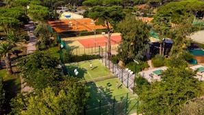Luchtbeeld van een tennisbaan, omringd door weelderige begroeiing en bomen, met een helder uitzicht over het omliggende landschap.