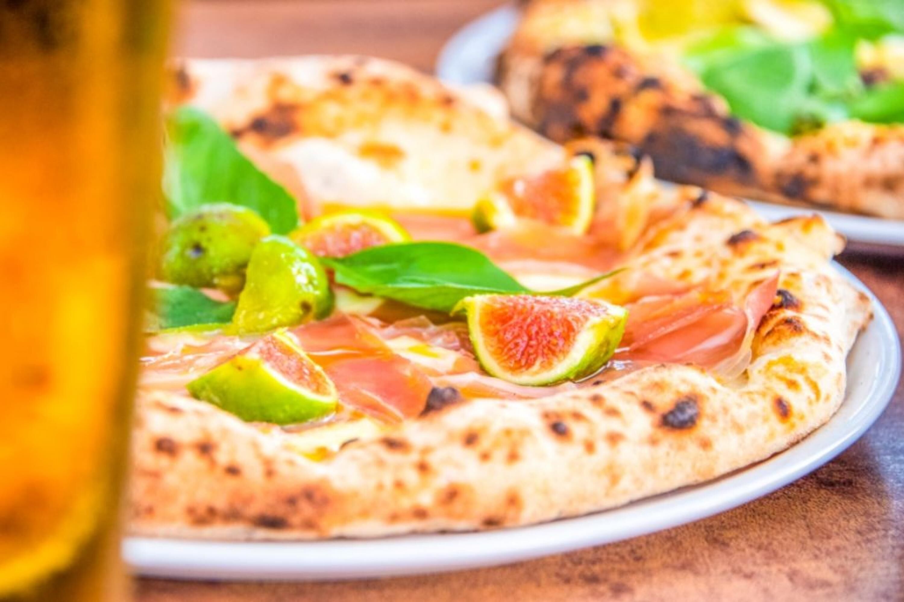A pizza with toppings like figs, prosciutto, and basil on a wooden table.