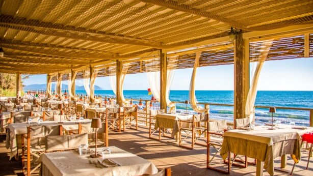 En udendørs restaurant med borde og stole, med udsigt over havet.
