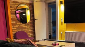 A modern living room with a sofa, a coffee table, a TV mounted on the wall, and a door leading to another room. - Rent a full equipped basement in a Design house only 15min from city center. (Gentofte)