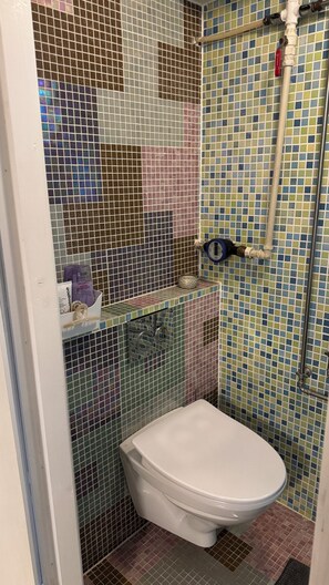 A bathroom with a toilet, a shower area, and a tiled wall. - Rent a full equipped basement in a Design house only 15min from city center. (Gentofte)
