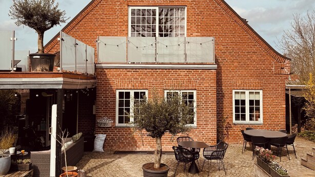 A brick house with a large window, a potted tree, and a patio with outdoor furniture. - Rent a full equipped basement in a Design house only 15min from city center. (Gentofte)