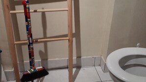 Une salle de bain avec une échelle en bois, un seau rouge et des toilettes.
