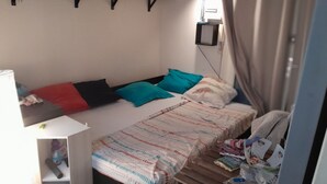 Une petite chambre avec un lit simple, une table de chevet et une petite étagère.