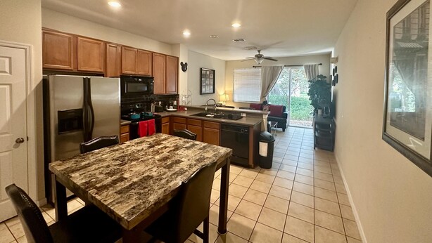 A modern kitchen with wooden cabinets, a stainless steel refrigerator, and a granite countertop. - Grand Panoramic 3BR Townhouse Near Disney (Kissimmee)