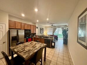 A modern kitchen with wooden cabinets, a stainless steel refrigerator, and a granite countertop. - Grand Panoramic 3BR Townhouse Near Disney (Kissimmee)