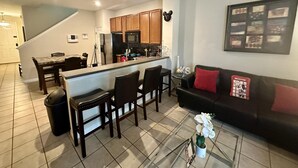 A modern kitchen with wooden cabinets, a central island, and a dining area with chairs. - Grand Panoramic 3BR Townhouse Near Disney (Kissimmee)