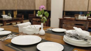 A dining table set with white plates, silverware, and a vase with a purple flower. - The Unalome Resort (Leh)