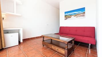 Una stanza con un divano rosso, un tavolino in legno, un armadietto bianco e un quadro raffigurante una spiaggia.
