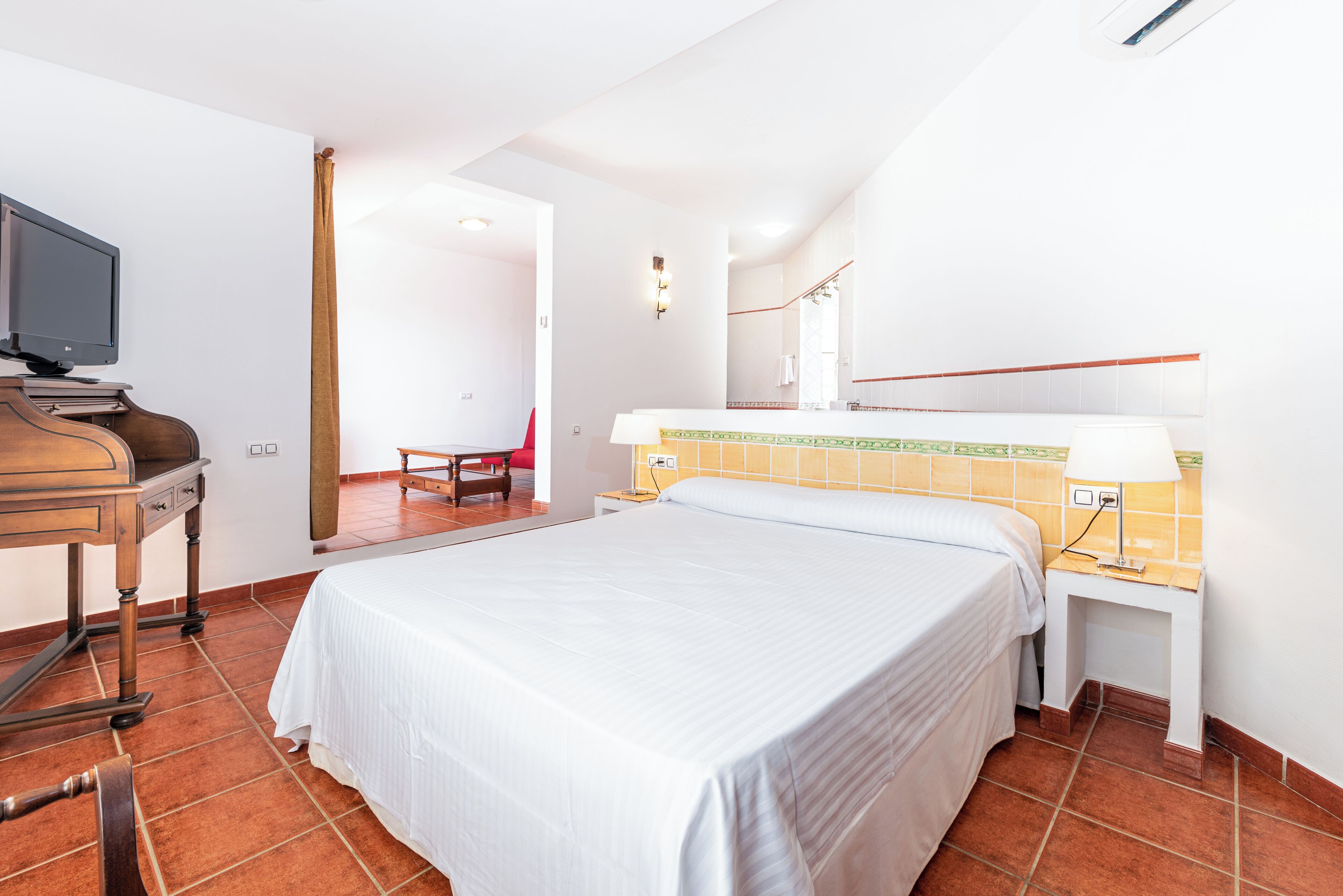 Una habitación de hotel con cama, escritorio, computadora, televisor y una silla.