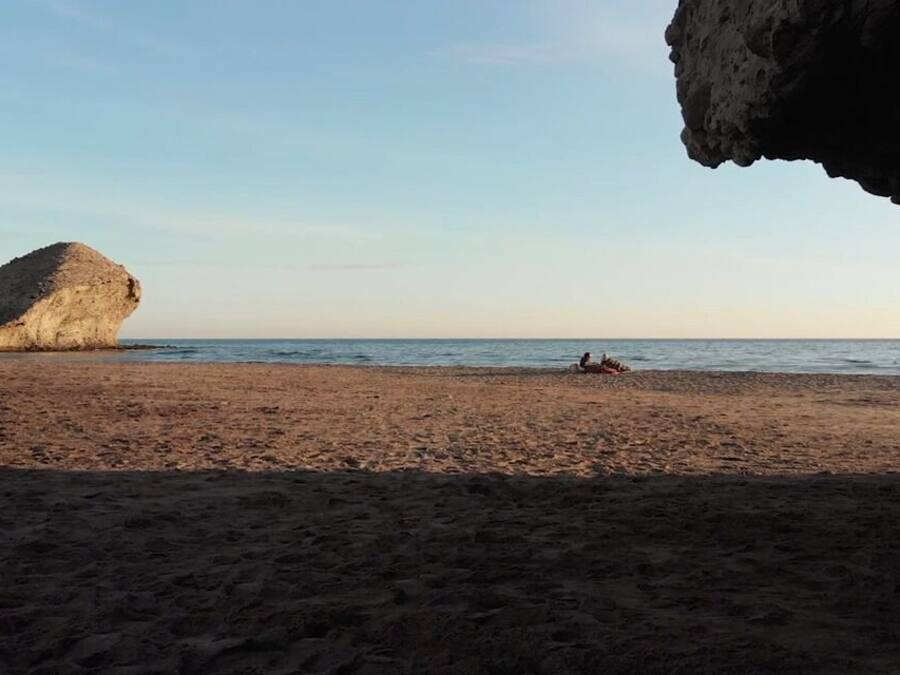 A beach with a large rock formation and a person lying on the sand.