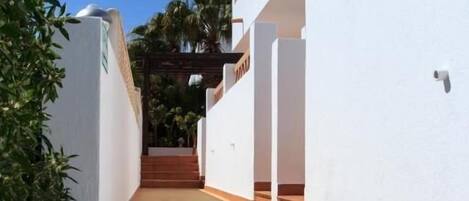 A set of outdoor stairs leading up to a building with white walls and a wooden railing.