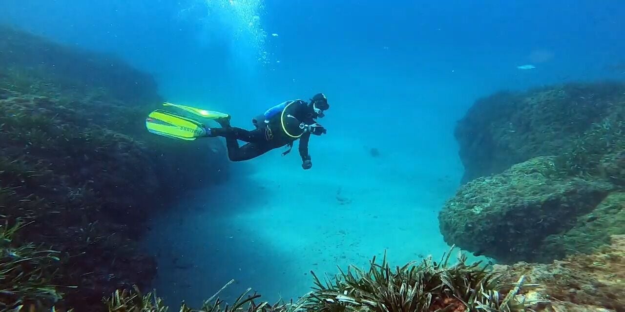 Un plongeur dans une grotte aux parois rocheuses, où la vie marine est peu abondante.