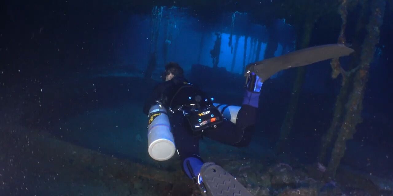 A diver in a dark underwater environment with a helmet and fins.
