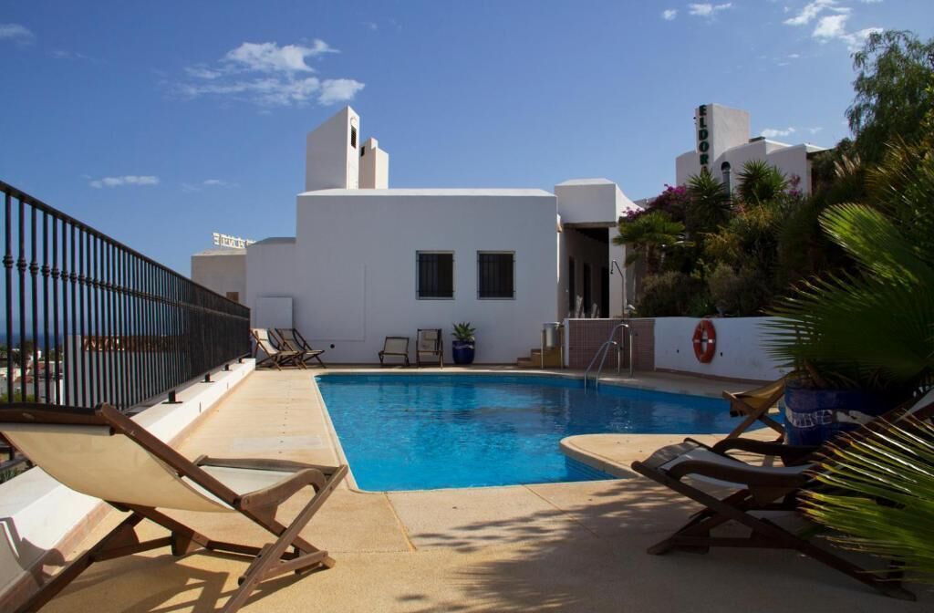 A pool area with lounge chairs, a lifebuoy, and a white building with a sign that reads "EL DORADO".