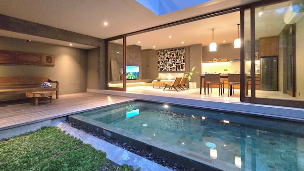 A modern house with a glass-enclosed living area, a pool, and a dining area with a kitchen visible through the glass. - Pulang Villas Private Pool Pererenan (Canggu)