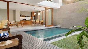 A modern outdoor pool area with a wooden deck, a dining area with chairs and a table, and a kitchen in the background. - Pulang Villas Private Pool Pererenan (Canggu)