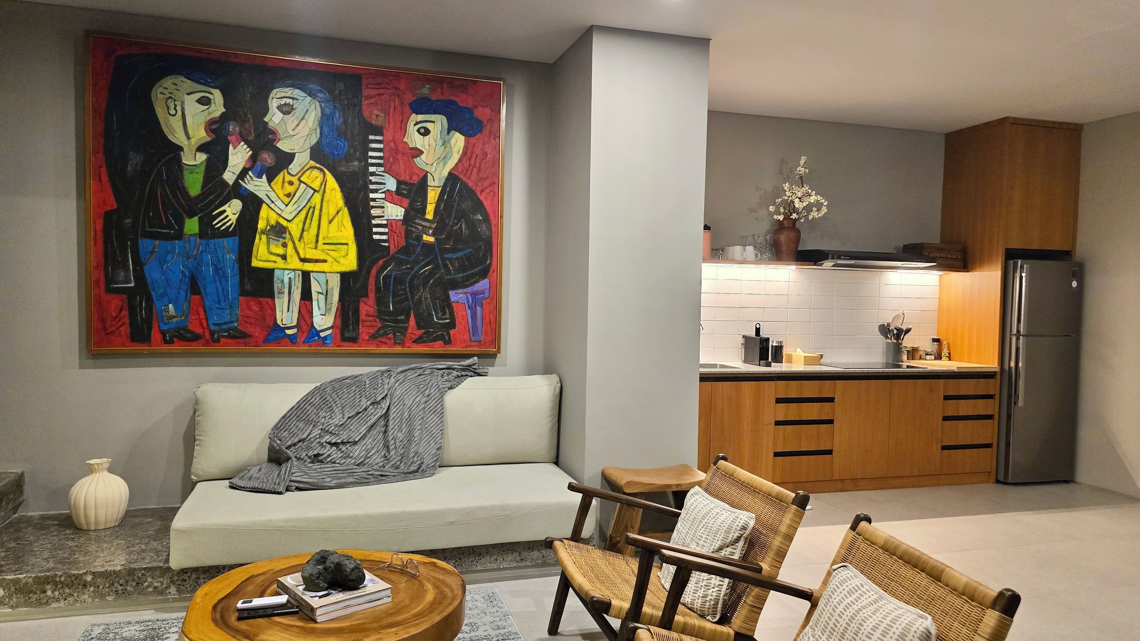 A modern living room with a sofa, two wicker chairs, a coffee table, and a painting on the wall.