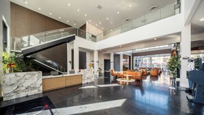 Un hall d’entrée spacieux avec un comptoir de réception en marbre, un escalier et un coin salon agrémenté de canapés orange.