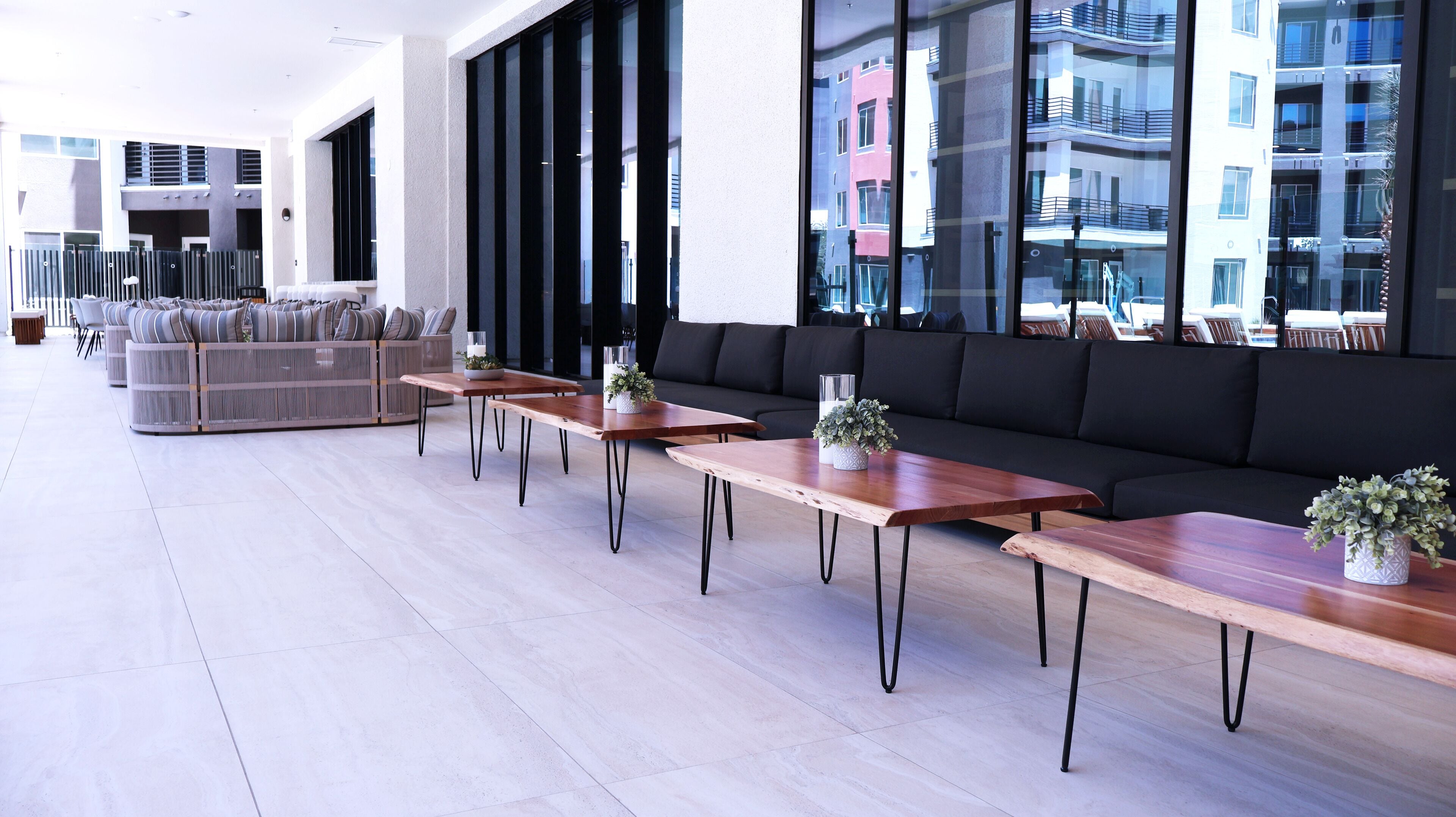 Un espace de détente moderne avec de longues tables en bois, des canapés noirs et des plantes en pot.