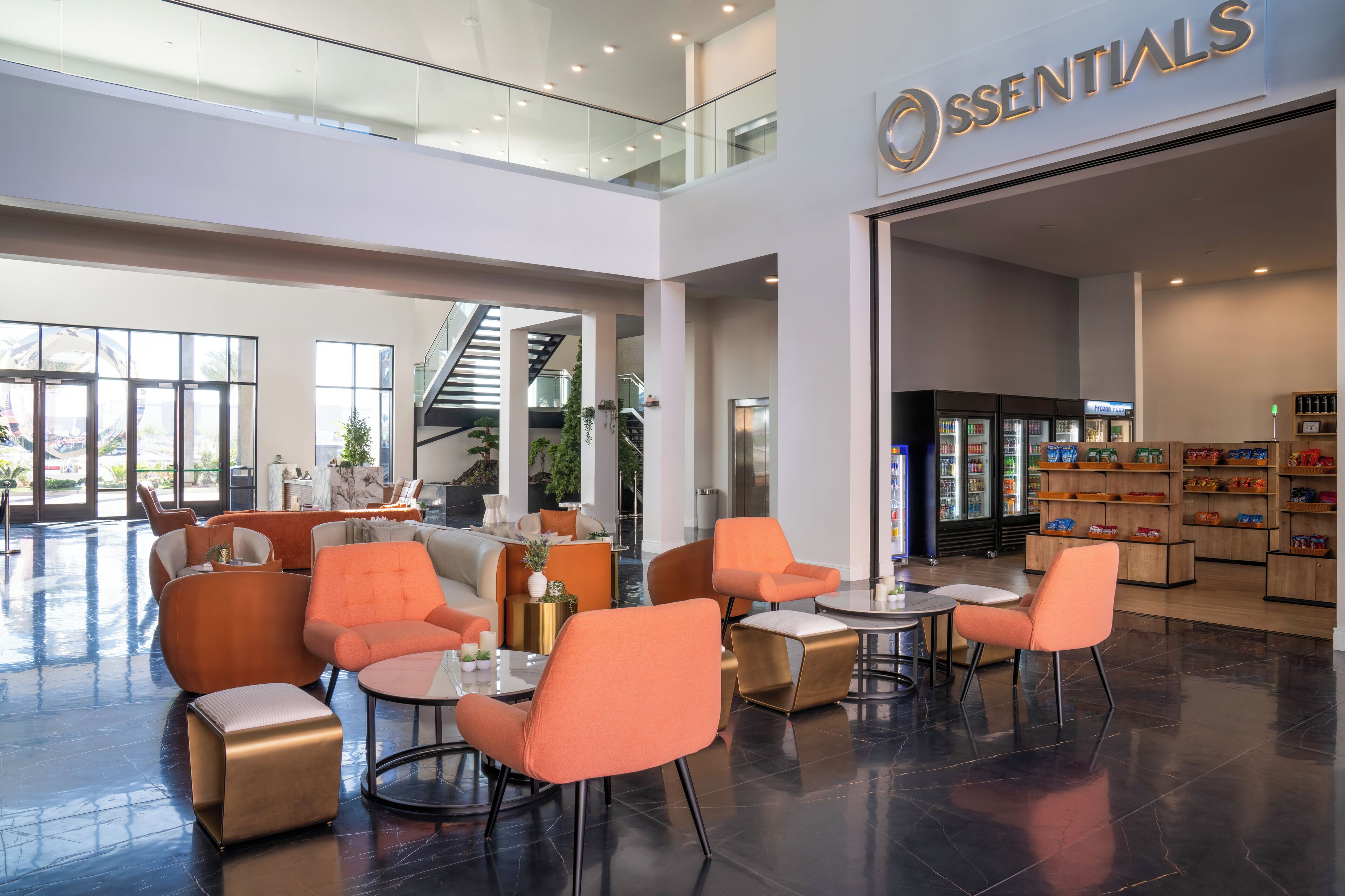 A modern hotel lobby with orange seating, a staircase, and a store named 'ESSENTIALS'.