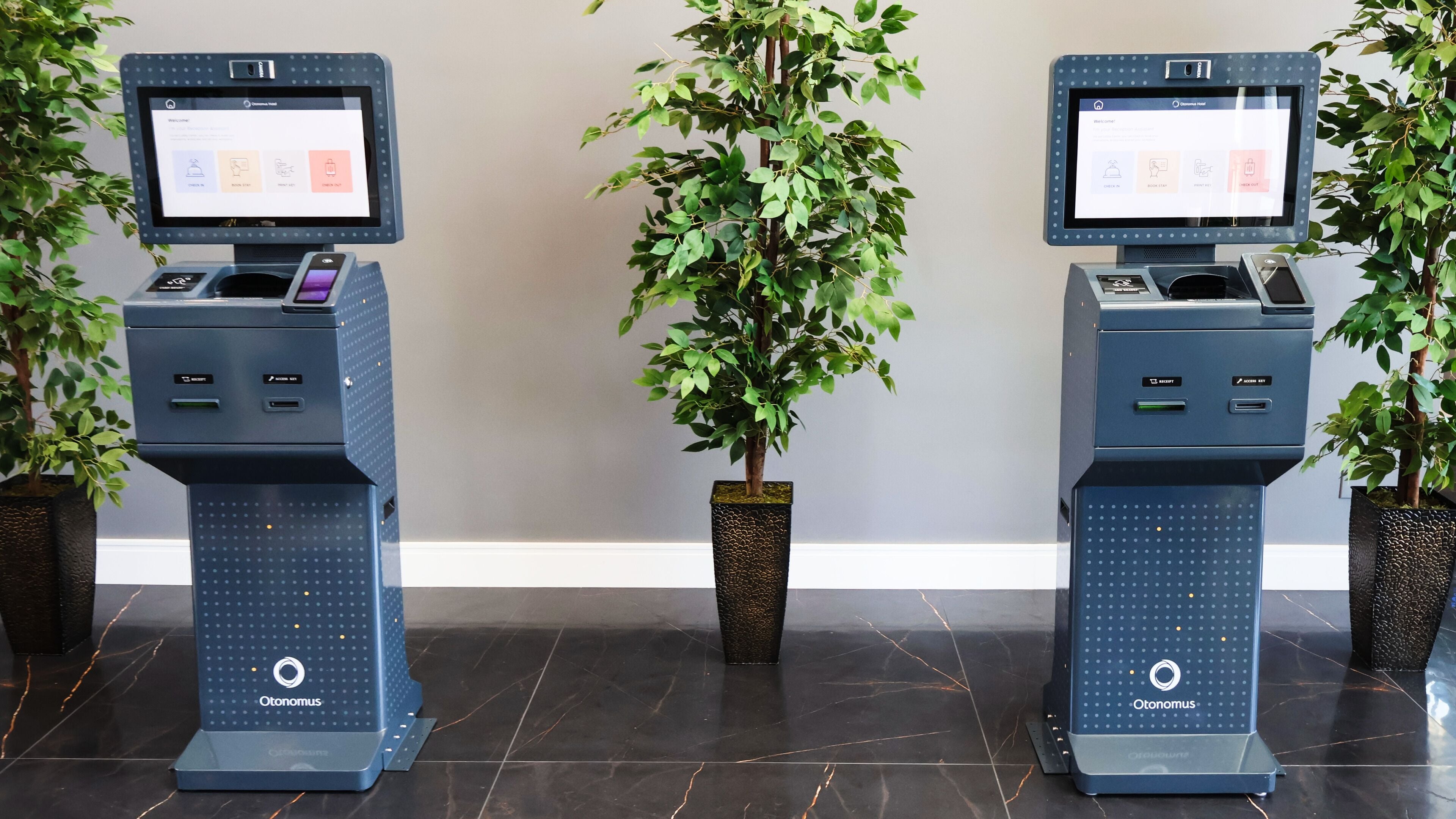 Deux bornes en libre-service équipées d’écrans, une plante en pot et un sol en marbre.