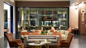 Un hall d’entrée moderne avec un espace salon comprenant des canapés et des fauteuils, un comptoir de réception et un mur de verre donnant sur le bar.