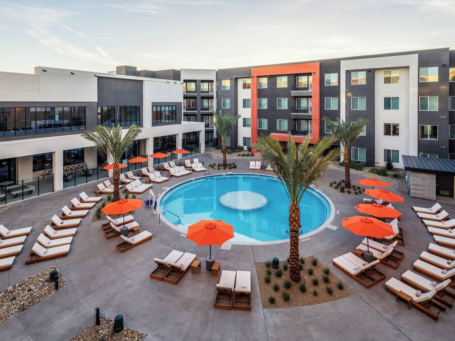 Een modern hotel met een centraal gelegen zwembad, ligbedden en palmbomen.
