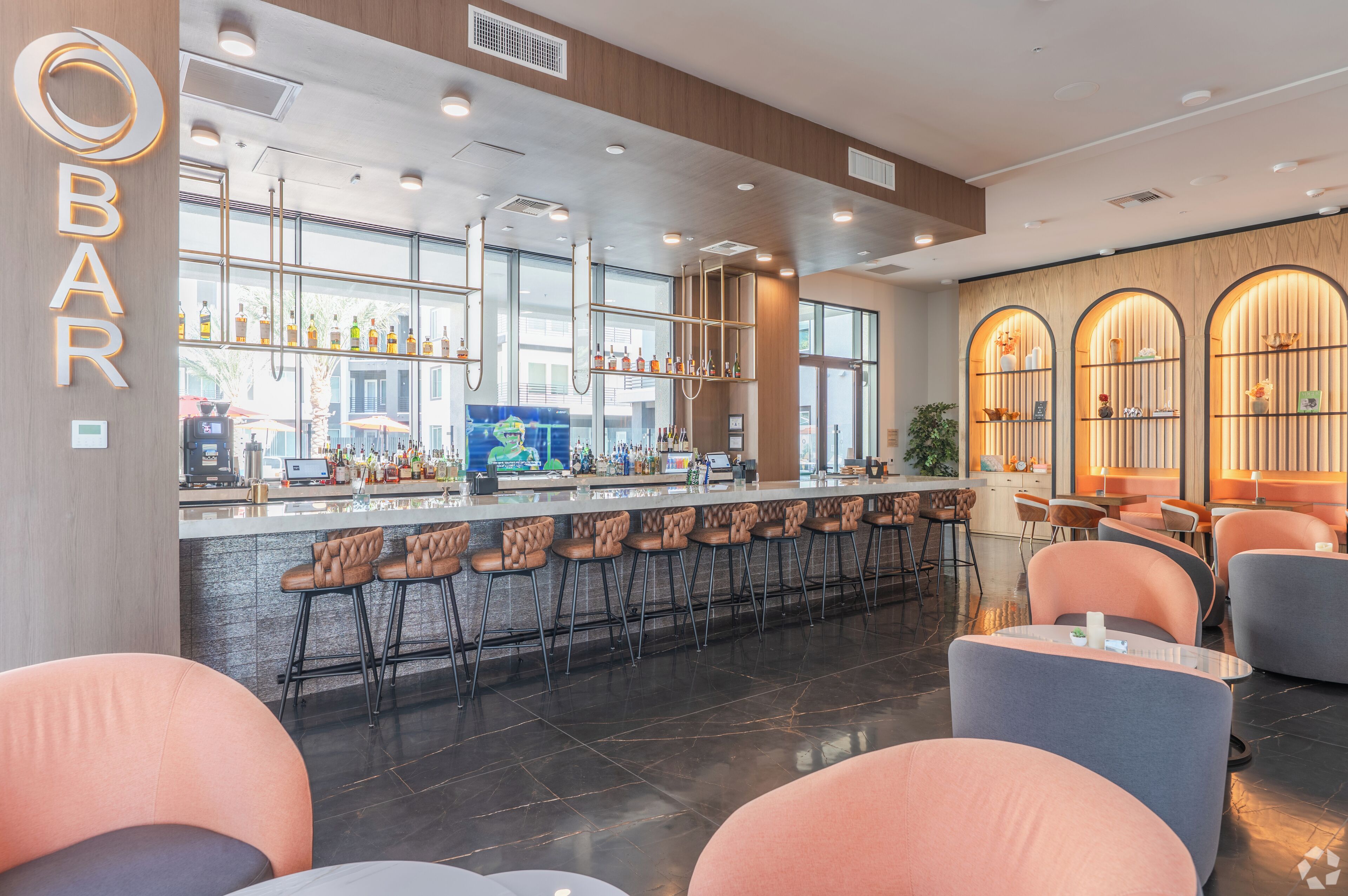 A modern bar area with a long counter, bar stools, and seating with tables.