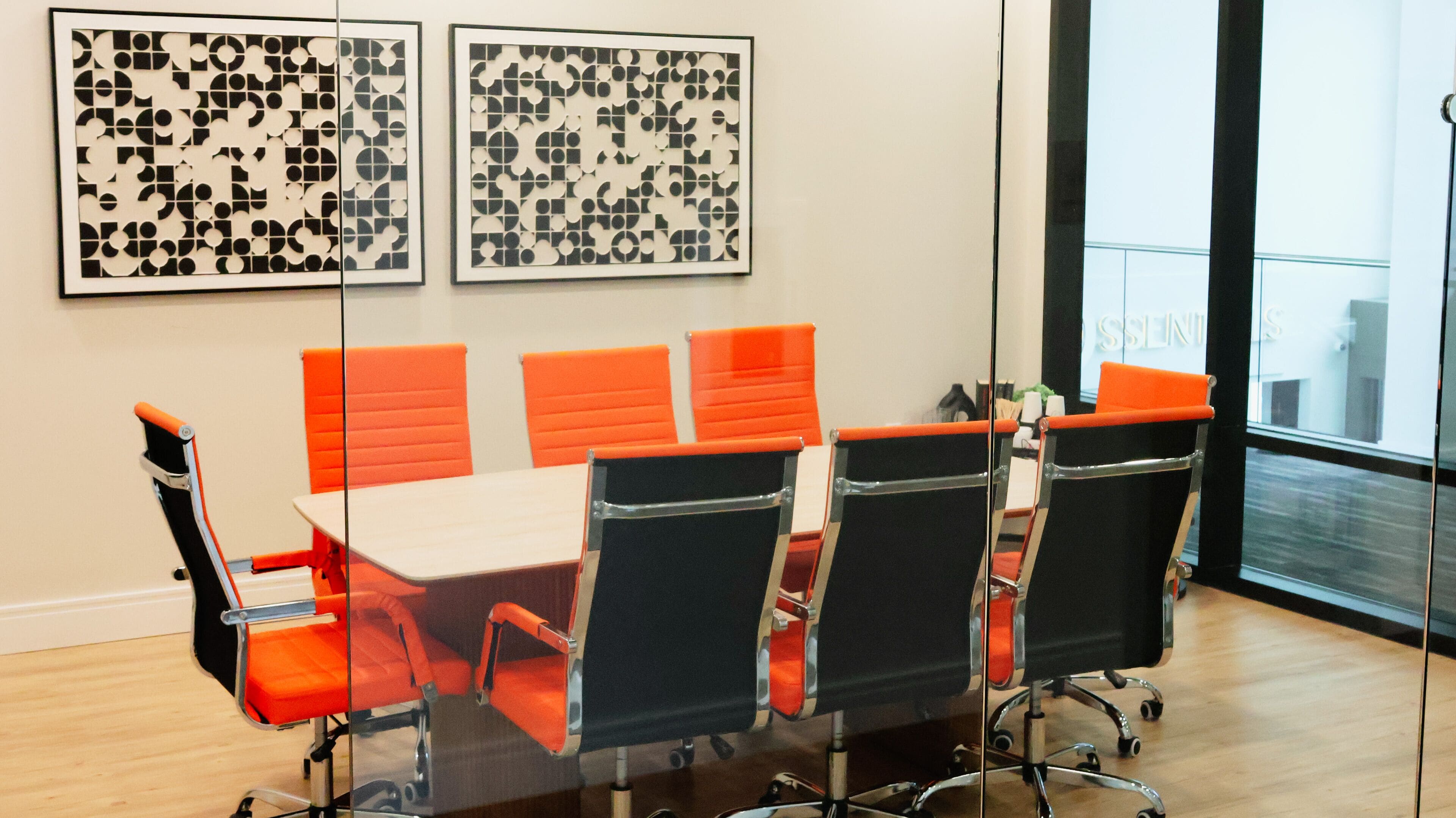 A conference room with a glass partition, orange chairs, and two framed abstract artworks on the wall.