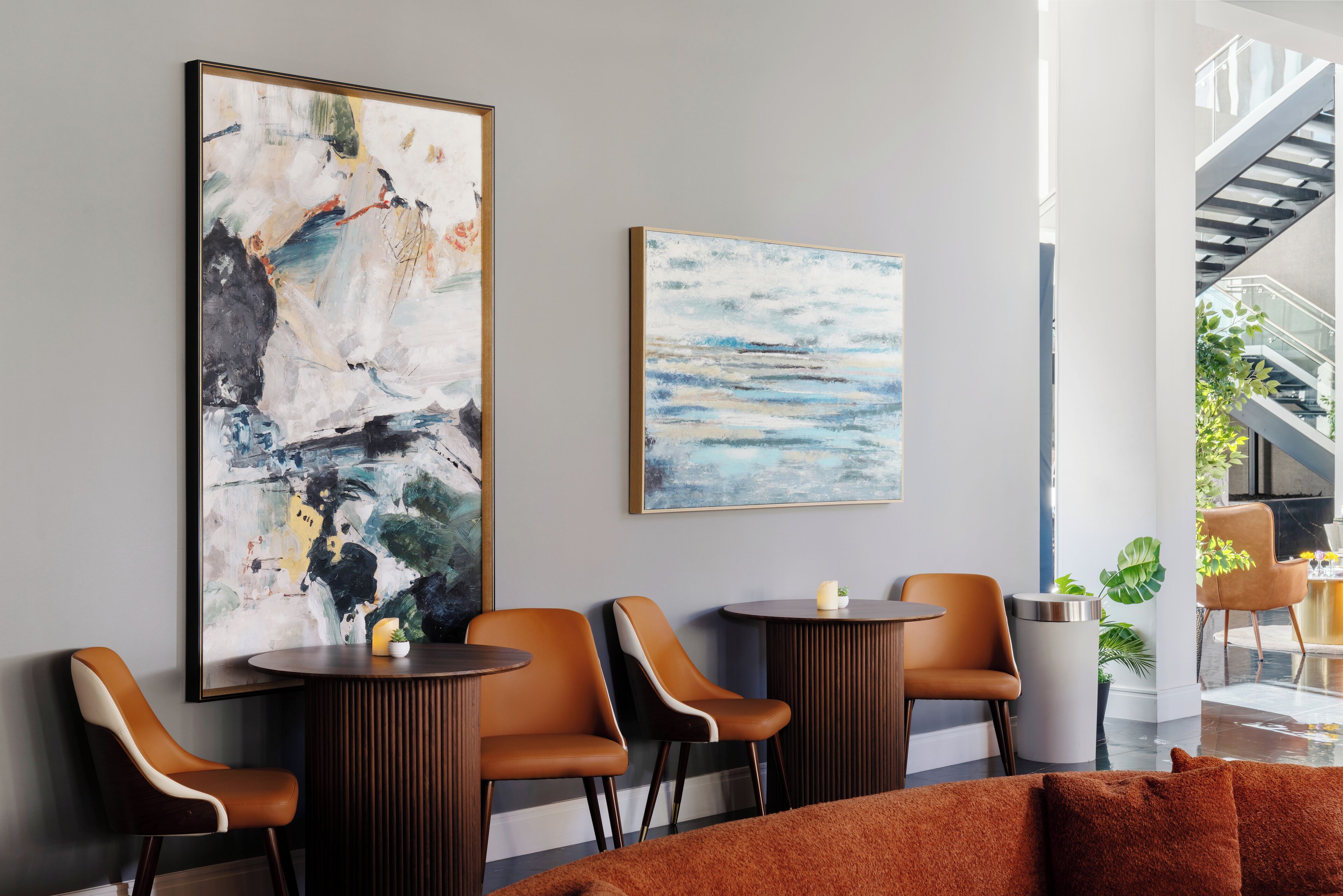 Un interior moderno con pinturas abstractas, sillas de cuero, una mesa redonda y una escalera.