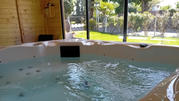 Ein Whirlpool mit einem schwarzen Gegenstand darin, Holzwänden und Blick auf Grünfläche.