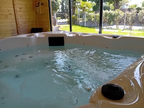 A hot tub with a black object inside, wooden walls, and a view of greenery outside.