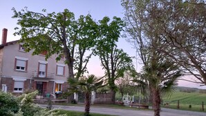 Ein zweistöckiges Haus mit Balkon, umgeben von Bäumen und einer grünen Rasenfläche.