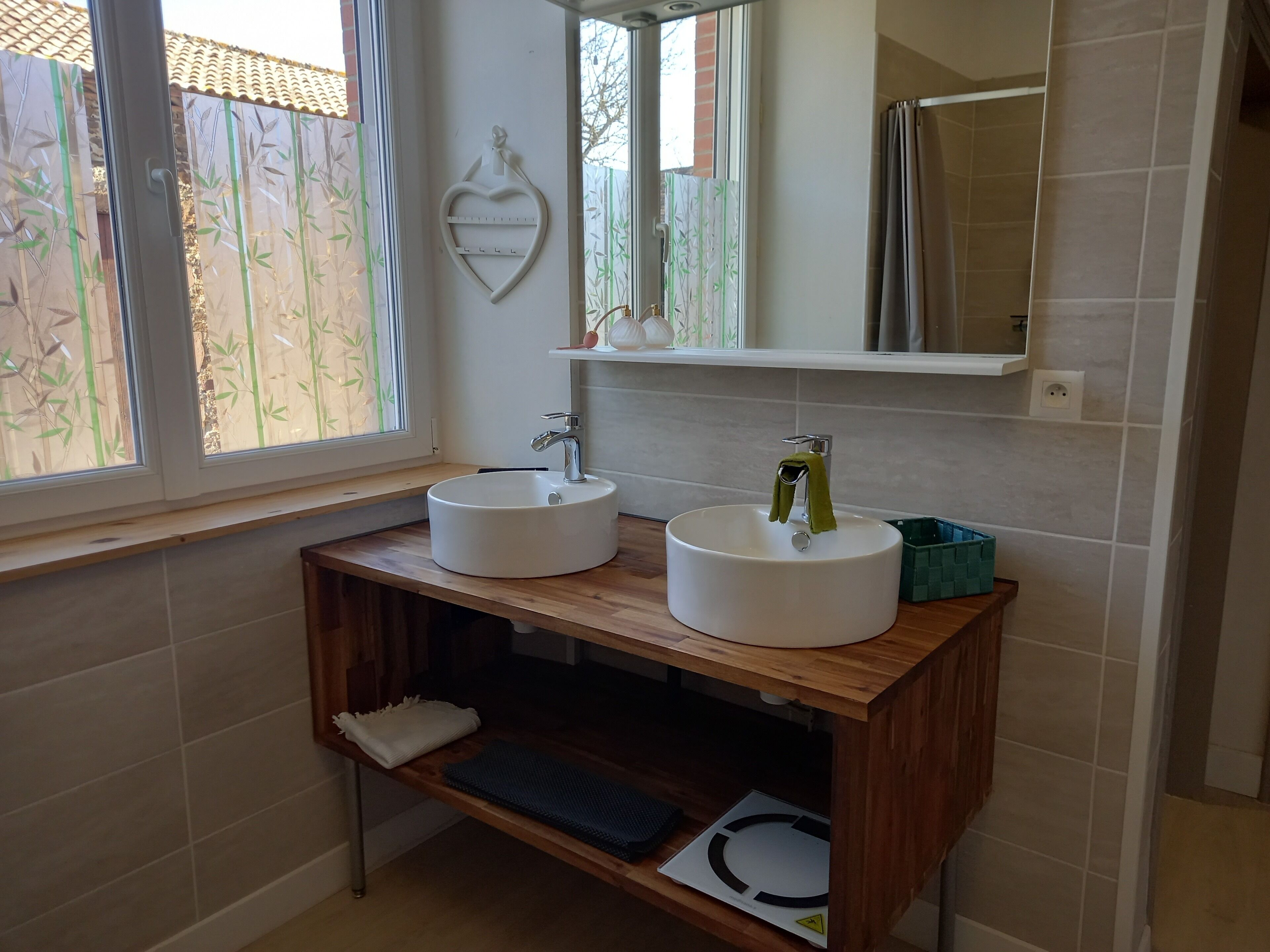 A bathroom with two sinks, a mirror, and a window with bamboo-patterned blinds.