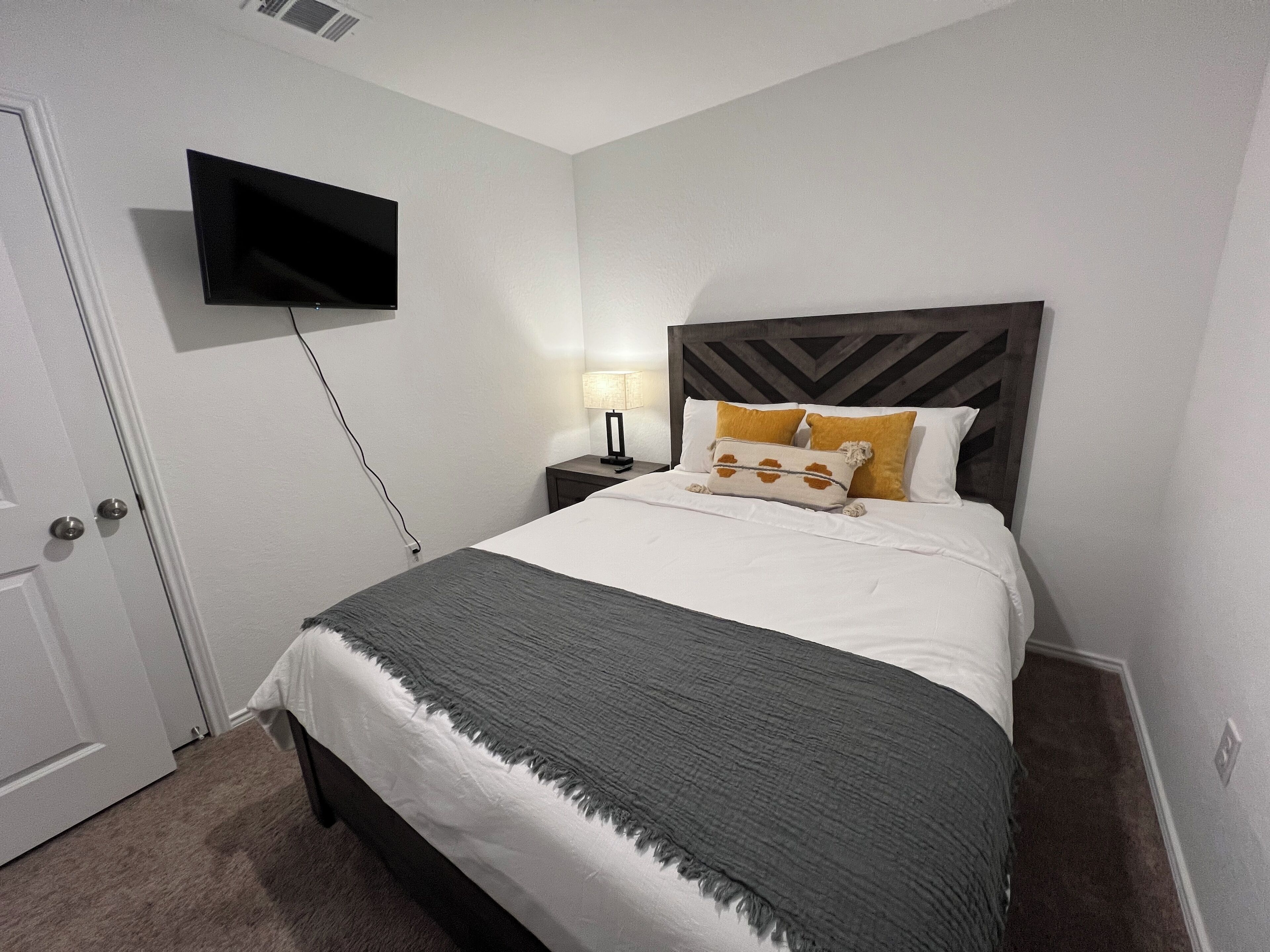 A neatly made bed with a grey blanket, a bedside lamp, and two pillows with a brown and white pattern.