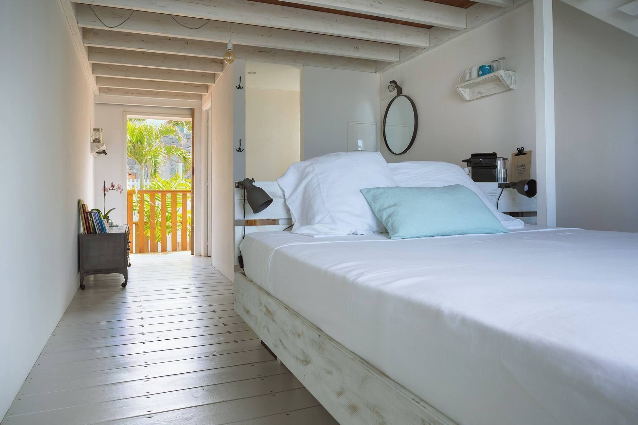 A bedroom with a bed, a desk, a chair, a shelf, and a view of the outdoors.