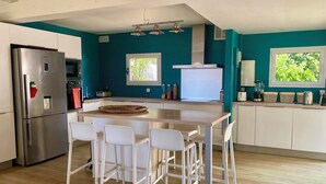 Eine moderne Küche mit Kochinsel, weißen Stühlen, einem Edelstahlkühlschrank und teal-farbenen Wänden.