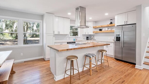A modern kitchen with white cabinets, a stainless steel refrigerator, and a wooden island with stools.