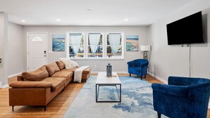 A modern living room with a brown sofa, blue armchairs, a coffee table, and a TV on the wall.