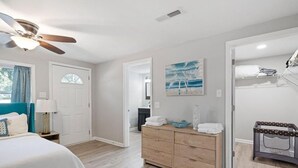 A bedroom with a bed, a dresser, a ceiling fan, and a door leading to another room.