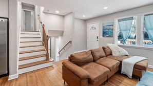 A living room with a brown sectional sofa, a wooden staircase, and a large window with curtains.