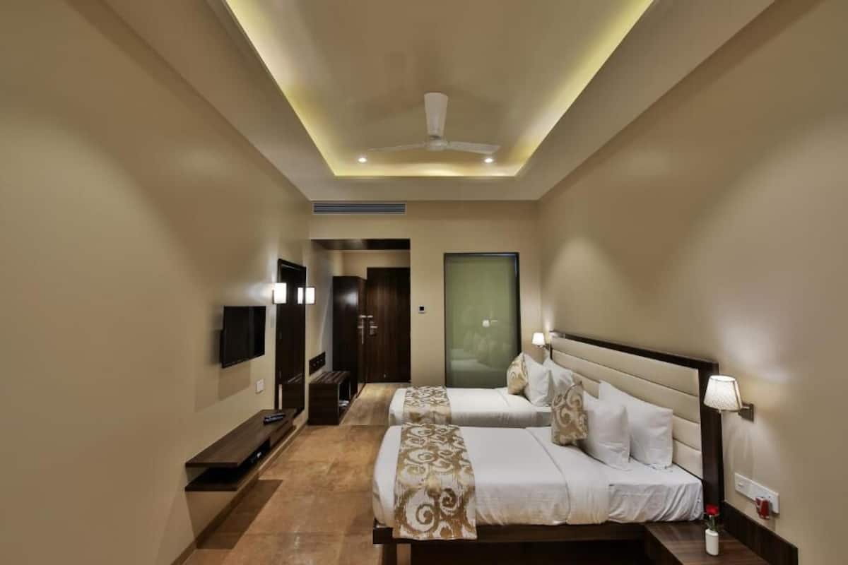 Quarto de hotel moderno com duas camas, uma televisão, um ventilador de teto e uma mesa de cabeceira com luminária.