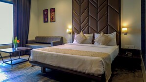 Quarto de hotel com uma cama grande, um sofá, uma mesinha e uma luminária fixada na parede.