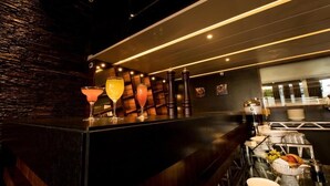 Uma área de bar com painel de madeira escura, balcão de vidro e variedade de bebidas.