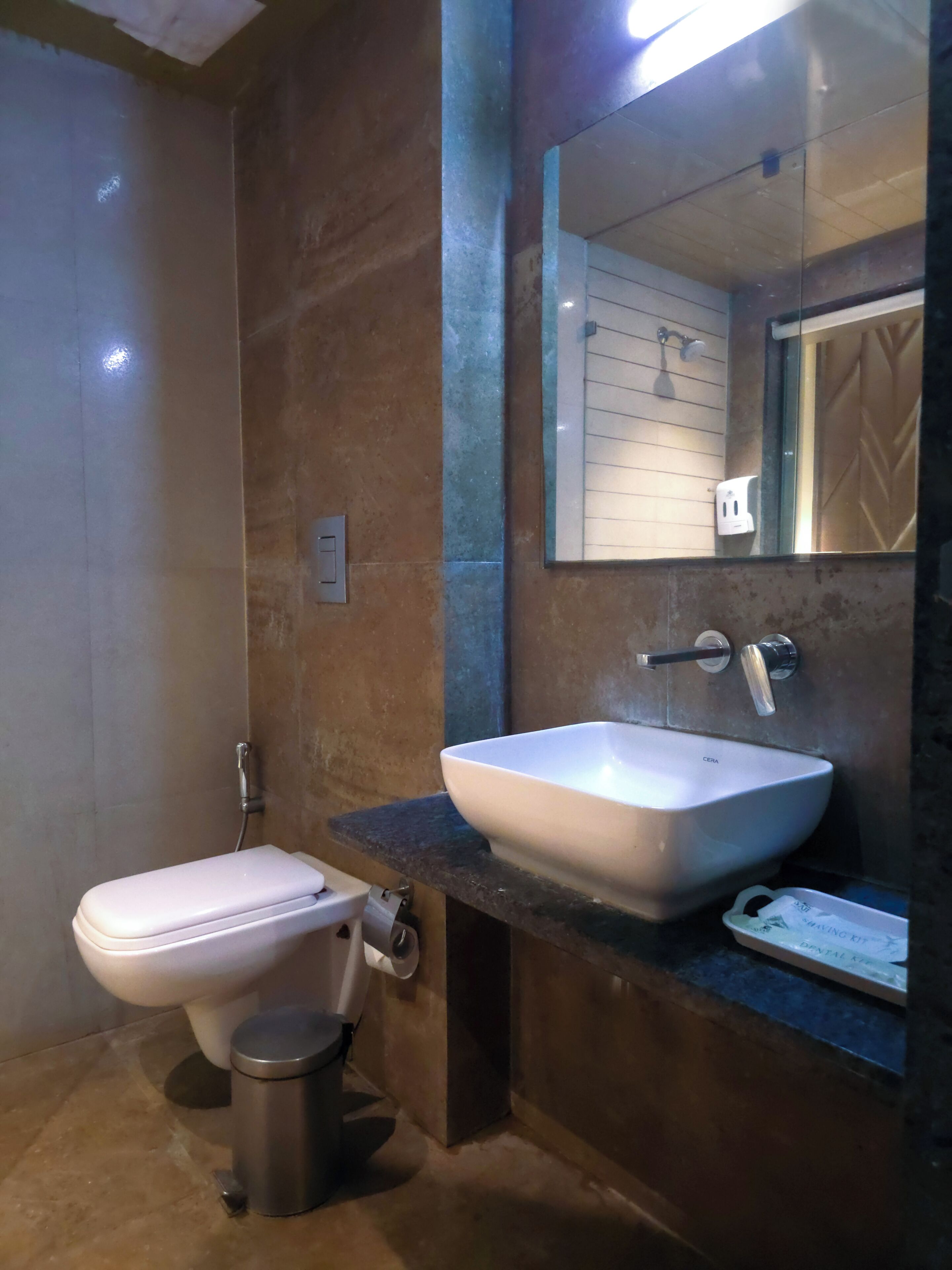 A modern bathroom with a white toilet, a sink with a mirror above it, and a trash bin.