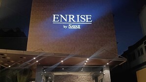 Exterior do hotel ENRISE by SAYALI, com uma placa visível e uma entrada moderna.