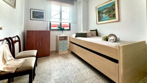 Un dormitorio con cama, una silla, un armario, una mesita de noche con un florero y una ventana con vista a un puente.